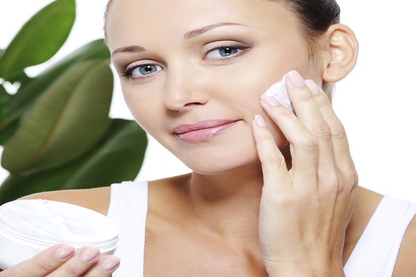 Portrait of health woman holding bottle with moisturizer cream and applying it on her face